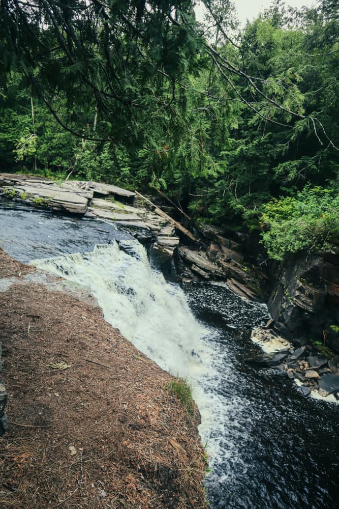 Canyon Falls pouring over a rock ledge into the Sturgeon River gorge beneath evergreens